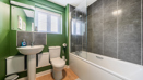 Bathroom with green walls, pedestal sink, toilet, and bathtub with shower screen.