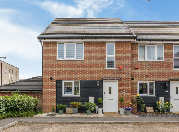 Brick semi-detached house with driveway, small front garden and blue sky.