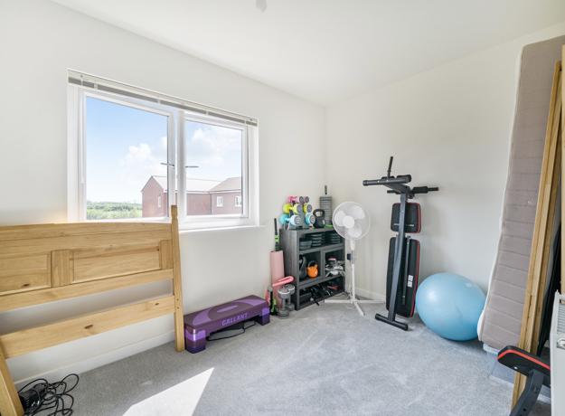 Bedroom with exercise equipment, dismantled bed and a large window.
