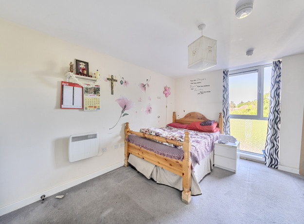 Bedroom with bed, desk area and window bringing in natural light