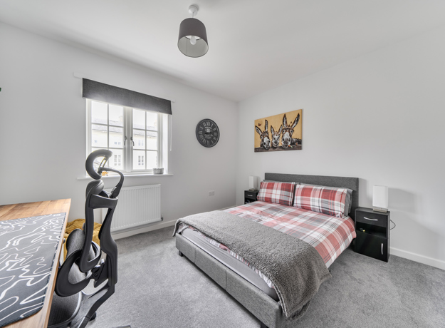 Bedroom with double bed, desk, and window with grey carpet.