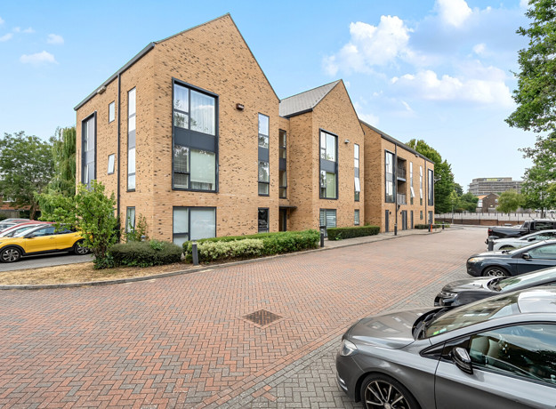 Modern apartment building with hedges, street and parked cars in front.