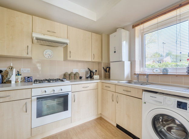 Kitchen with cabinets, oven, sink, boiler, washing machine and window.