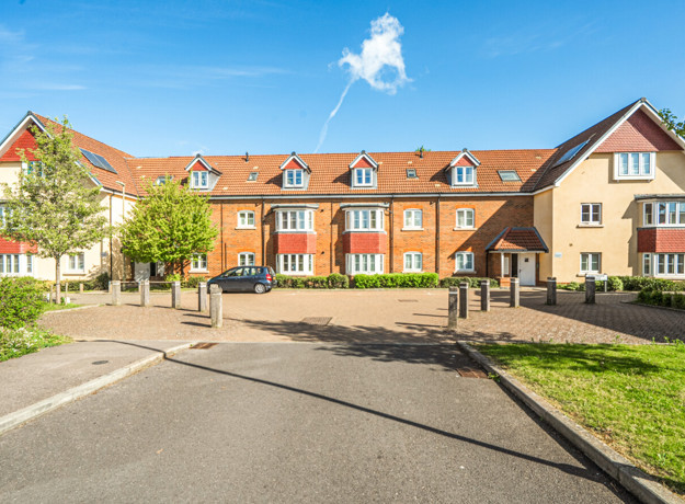 Exterior view of a three stories apartment building with red brick facade and landscaped grounds