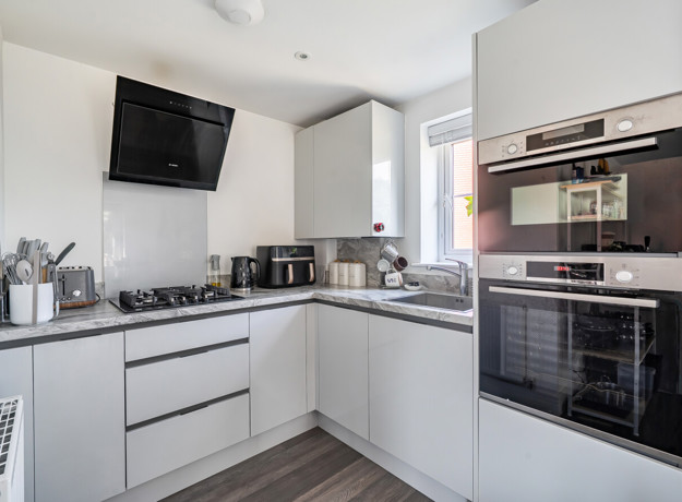 White kitchen with integrated appliances, hob, sink and wall-mounted extractor fan.