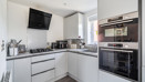 White kitchen with integrated appliances, hob, sink and wall-mounted extractor fan.