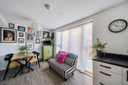 Living room with striped sofa, dining table with chairs, plants, and wall photos near large window.