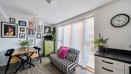 Living room with striped sofa, dining table with chairs, plants, and wall photos near large window.