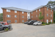 Brick apartment building with a paved parking area and several parked cars.