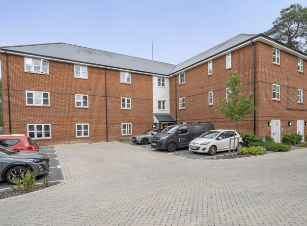 Brick apartment building with a paved parking area and several parked cars.