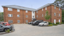 Brick apartment building with a paved parking area and several parked cars.