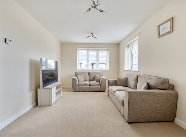 Living room with beige sofas, carpet, television, and windows letting in light.