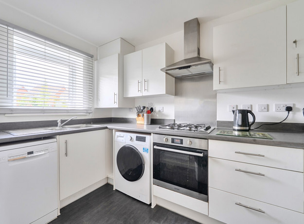 Kitchen with white cabinets, oven, washing machine and countertop appliances.