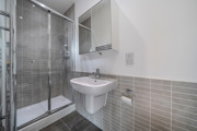 Modern shower room with glass shower enclosure, wall-mounted sink, toilet, and tiled walls