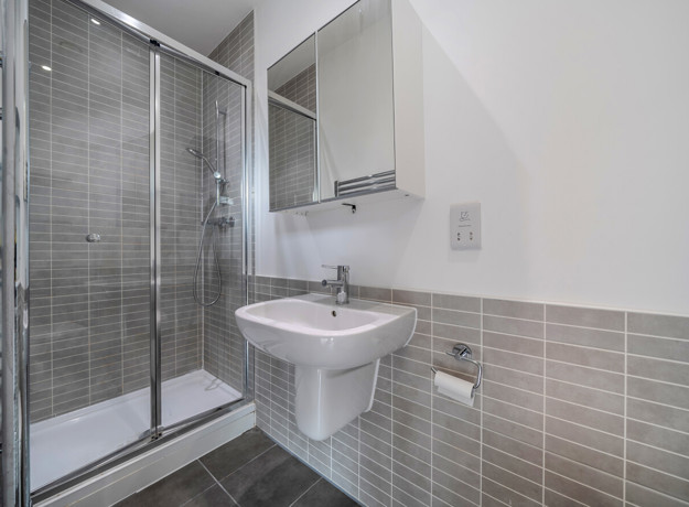 Modern shower room with glass shower enclosure, wall-mounted sink, toilet, and tiled walls