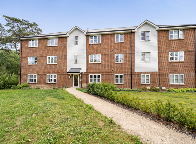 Three-storey brick apartment building with a path leading across a grass lawn.
