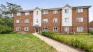 Three-storey brick apartment building with a path leading across a grass lawn.