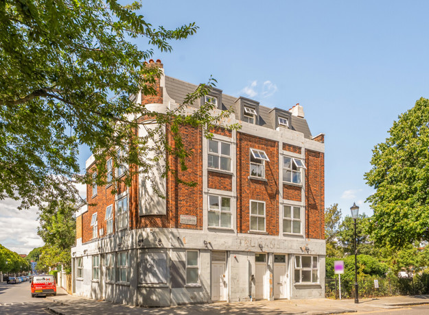 Corner view of a red brick apartment building beside a tree-lined street.