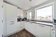 Fitted kitchen with white cabinets, integrated appliances and a window.