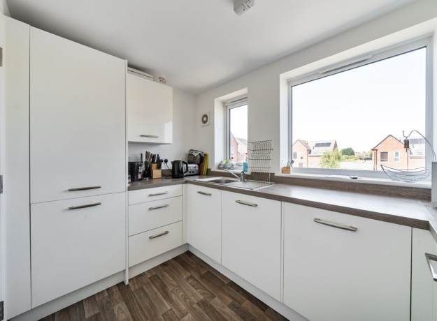 Fitted kitchen with white cabinets, integrated appliances and a window.