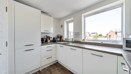 Fitted kitchen with white cabinets, integrated appliances and a window.