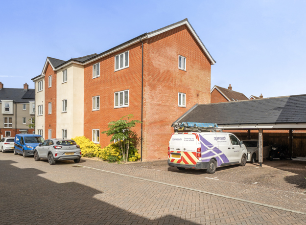 Exterior view of apartment block from parking area with cars and clear sky.
