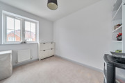 Empty bedroom with window, radiator, dresser and built in shelving.