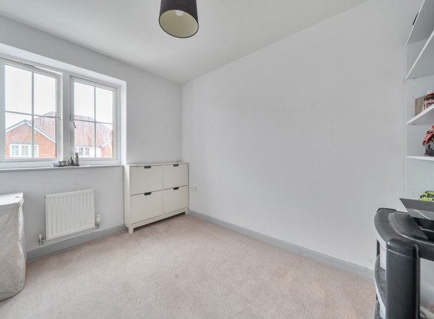 Empty bedroom with window, radiator, dresser and built in shelving.
