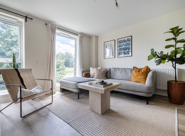 Living room with sofa, armchair, coffee table, large windows, and indoor plant.