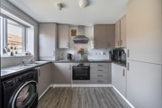 Kitchen with light grey cabinets, dark countertops, appliances and large window.