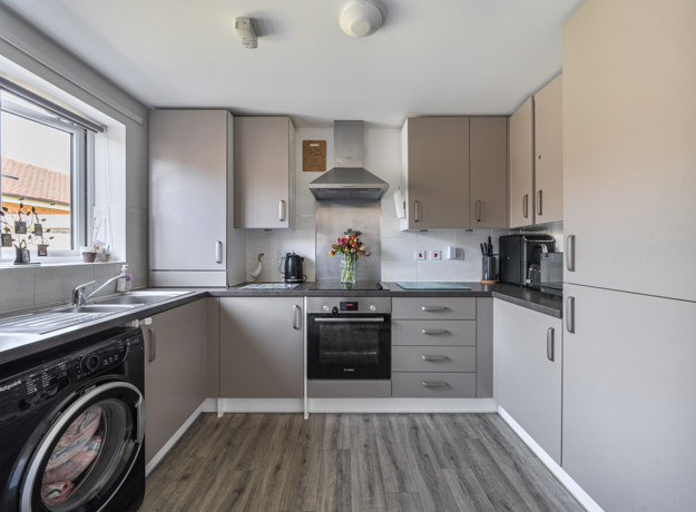 Kitchen with light grey cabinets, dark countertops, appliances and large window.