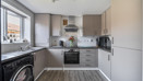 Kitchen with light grey cabinets, dark countertops, appliances and large window.