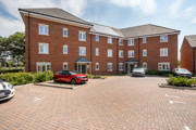 Back of apartment building with parked cars and paved courtyard.