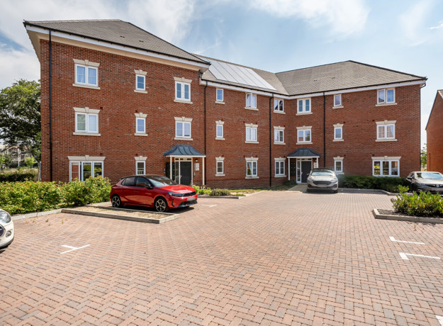 Back of apartment building with parked cars and paved courtyard.