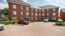 Back of apartment building with parked cars and paved courtyard.