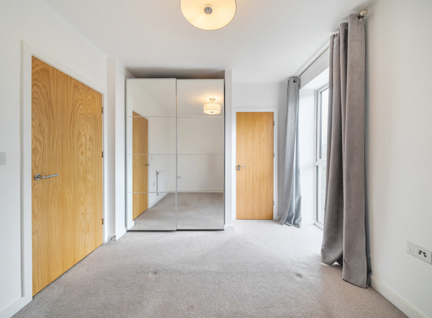 Carpeted bedroom with wooden doors, wardrobe with mirrored sliding doors and a ceiling light