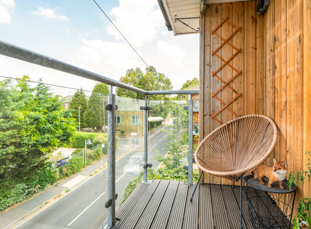 Balcony with glass railing, wooden cladding and a chair.