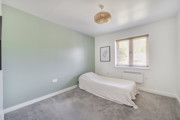 Double bedroom with soft green walls, carpeted floor and window letting in natural light
