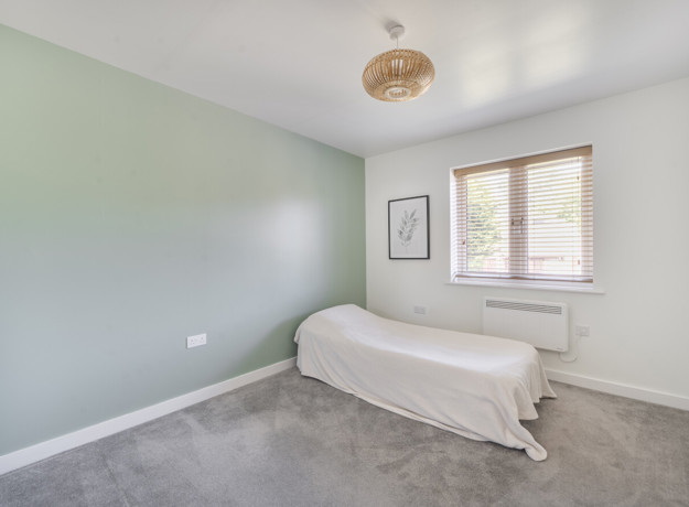 Double bedroom with soft green walls, carpeted floor and window letting in natural light