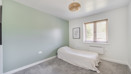 Double bedroom with soft green walls, carpeted floor and window letting in natural light