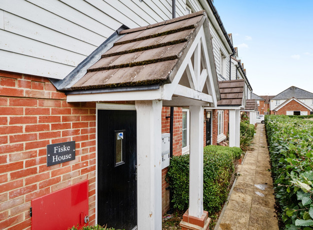 Red brick house entrance with white porch and narrow path along building.