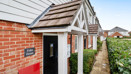 Red brick house entrance with white porch and narrow path along building.