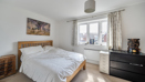 Spacious bedroom with double bed, dresser, and window letting in light.