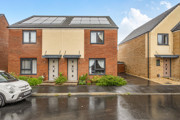 Row of modern brick houses with parking spaces and wet road in front.