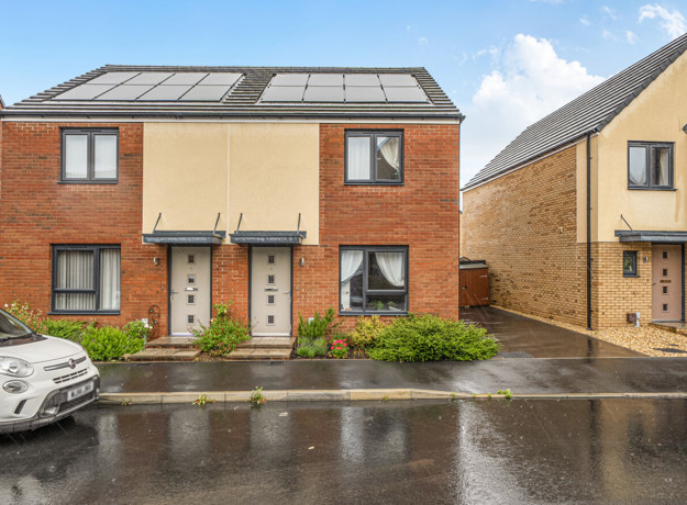 Row of modern brick houses with parking spaces and wet road in front.