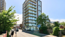 Modern high-rise apartment building on a street with balconies and surrounding greenery