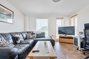 Open-plan living area with sofas, TV and large windows.