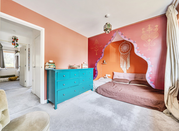 Bedroom with a bed, turquoise chest of drawers and decorative wall mural.