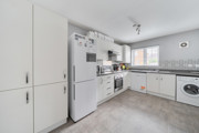 White fitted kitchen with appliances, cabinets and a window letting in daylight.