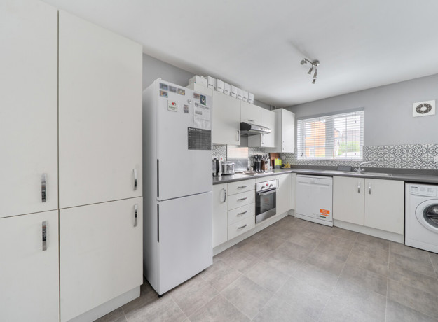White fitted kitchen with appliances, cabinets and a window letting in daylight.